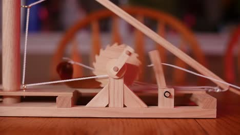 slow motion: close up of a toy wooden trebuchet firing on a wooden table with a chair and counter in the background