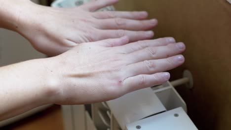 a woman warms hands on a battery at home in a room. 4k. close up. slow motion