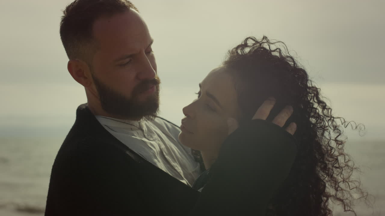 Pareja joven coqueteando en la playa en una cita romántica. Personas encantadoras tocando el cabello rizado junto al mar.