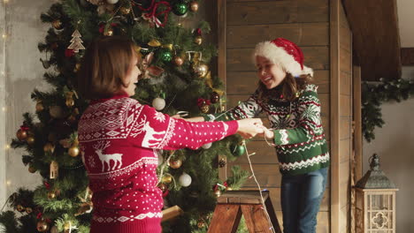 madre feliz e hija bailando y jugando juntas con luces mientras decoran el árbol de navidad en casa 2
