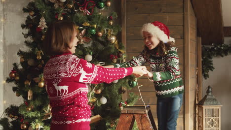 happy mom and daughter dancing and playing together with lights while decorating christmas tree at home 2