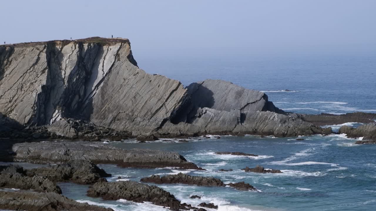 Blue ocean waves crash gently on jagged rock coastline of Portugal