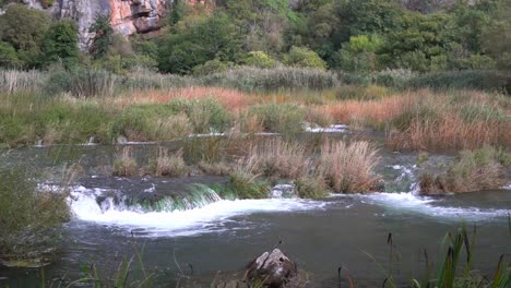 Short-but-wide-and-strong-waterfalls-from-one-pond-to-another-passing-through-grass-in-Krka-National-Park-in-Croatia-at-¼-speed