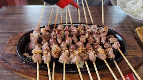 freshly cooked goat satay on hot plate being topped with soy sauce, close up