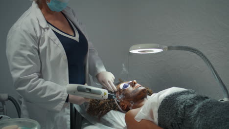 dermatólogo haciendo peeling facial con máscara de carbono. mujer acostada con gafas