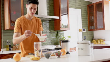 biracial man preparing fruit smoothie adding yoghurt to blender in kitchen, copy space, slow motion