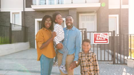 portrait of happy african american family with small children standing at new house at suburb and looking at camera