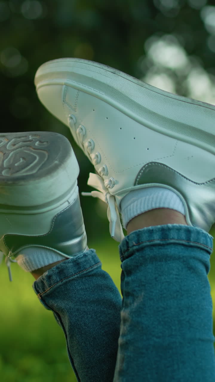 primer plano de zapatillas blancas con las piernas cruzadas en un campo cubierto de hierba con un fondo bokeh suave, la postura relajada y el atuendo casual crean un ambiente de ocio al aire libre rodeado de vegetación