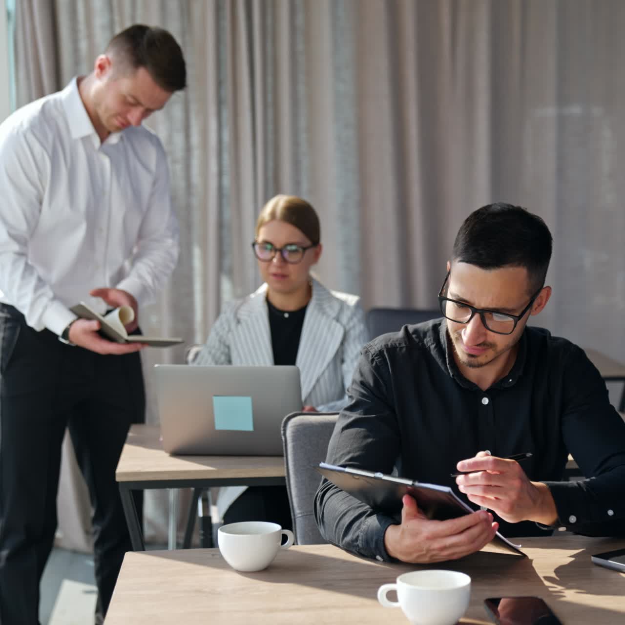 Male manager standing at the desk of female employee checking the data in his notebook. Male brunet colleague focused on the screen of his laptop
