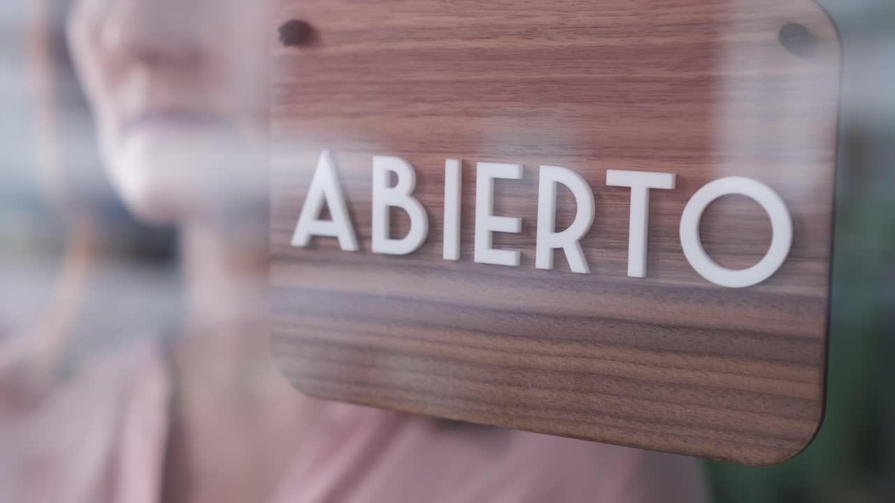 woman changing open to closed sign in spanish on window for corona virus pandemic.