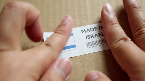 Hands-applying-MADE-IN-ISRAEL-flag-label-on-a-shipping-box-with-product-premium-quality-barcode