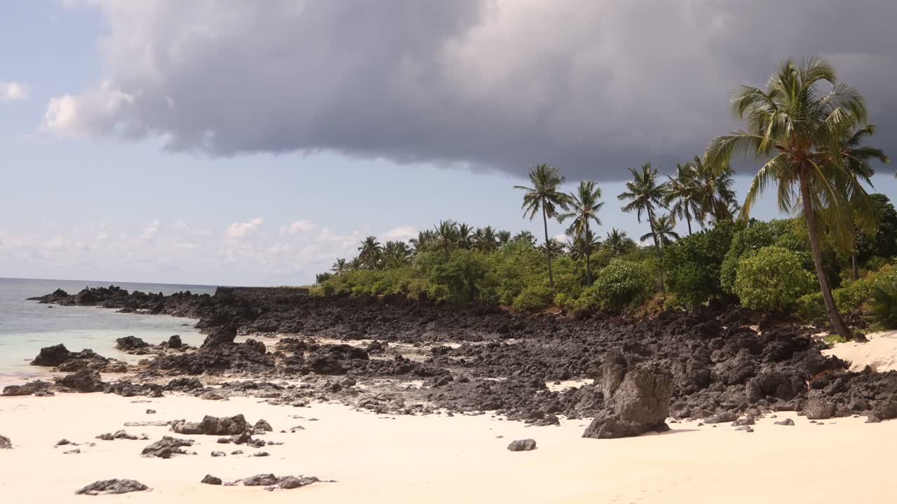 A serene tropical beach with white sand and rocky coastline on a sunny day.
