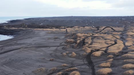 dunas cubiertas de hierba en la playa de arena volcánica negra sandvik con huellas de neumáticos de motocross