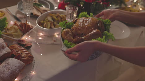 unrecognizable woman putting roast chicken on christmas dinner table 1