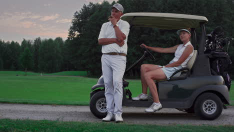 golf players sit cart on course. sport couple enjoy activity in driving golf car