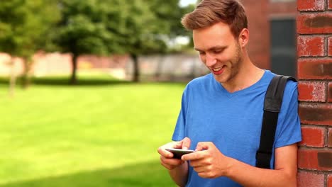 happy student texting on his phone outside