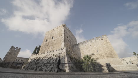 a person walks past the ancient stone fortifications of jerusalem under a bright sky, highlighting the city's monumental architecture and historical significance