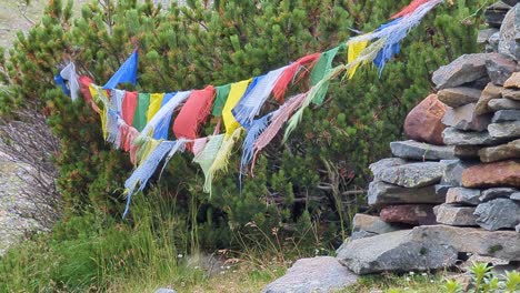 close up of worn out nepalese prayer flags in the wind in front of stones and bushes