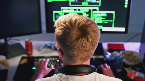 rear view of male teenage hacker sitting in front of computer screens bypassing cyber security