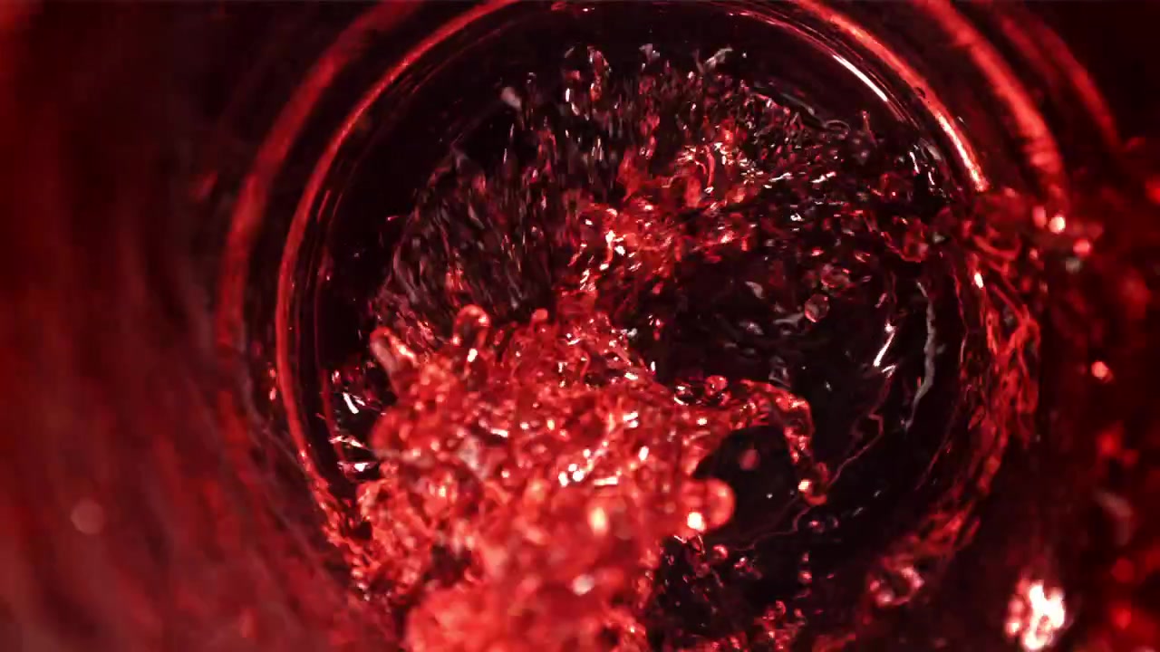 Liquido rosso che si versa e schizza in un bicchiere al rallentatore.