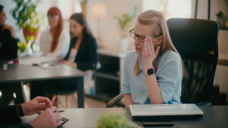 businesswoman explaining colleague at desk in office.