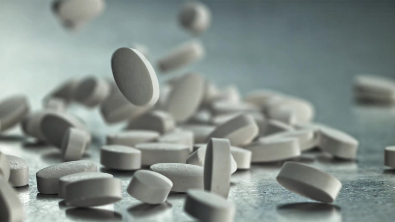 Primo piano di pillole mediche bianche che cadono al rallentatore.