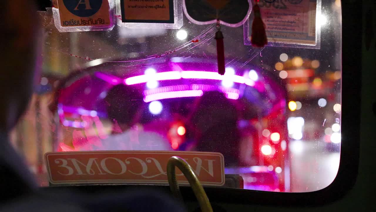 Vista del passeggero da un tuk-tuk che segue un veicolo al neon luminoso nel traffico notturno intenso della città.