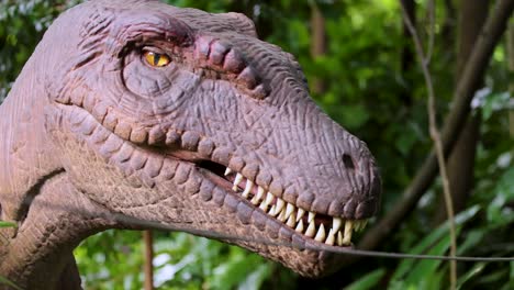 a realistic velociraptor animatronic head turns and moves in a dense, green outdoor park. natural daylight highlights detailed textures and lifelike motion