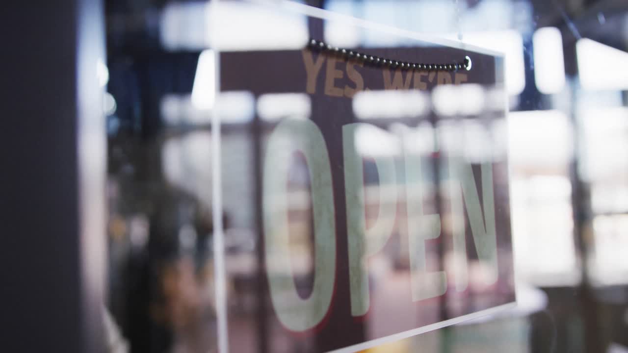 Close up of hands of female cafe owner changing closed sign to open in the window