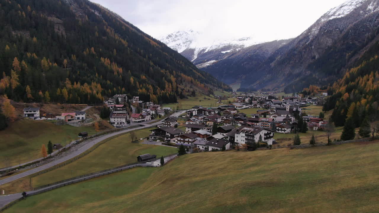 Volo aereo su campi rurali con un piccolo villaggio austriaco tra le montagne in autunno - Kauntertal, Austria