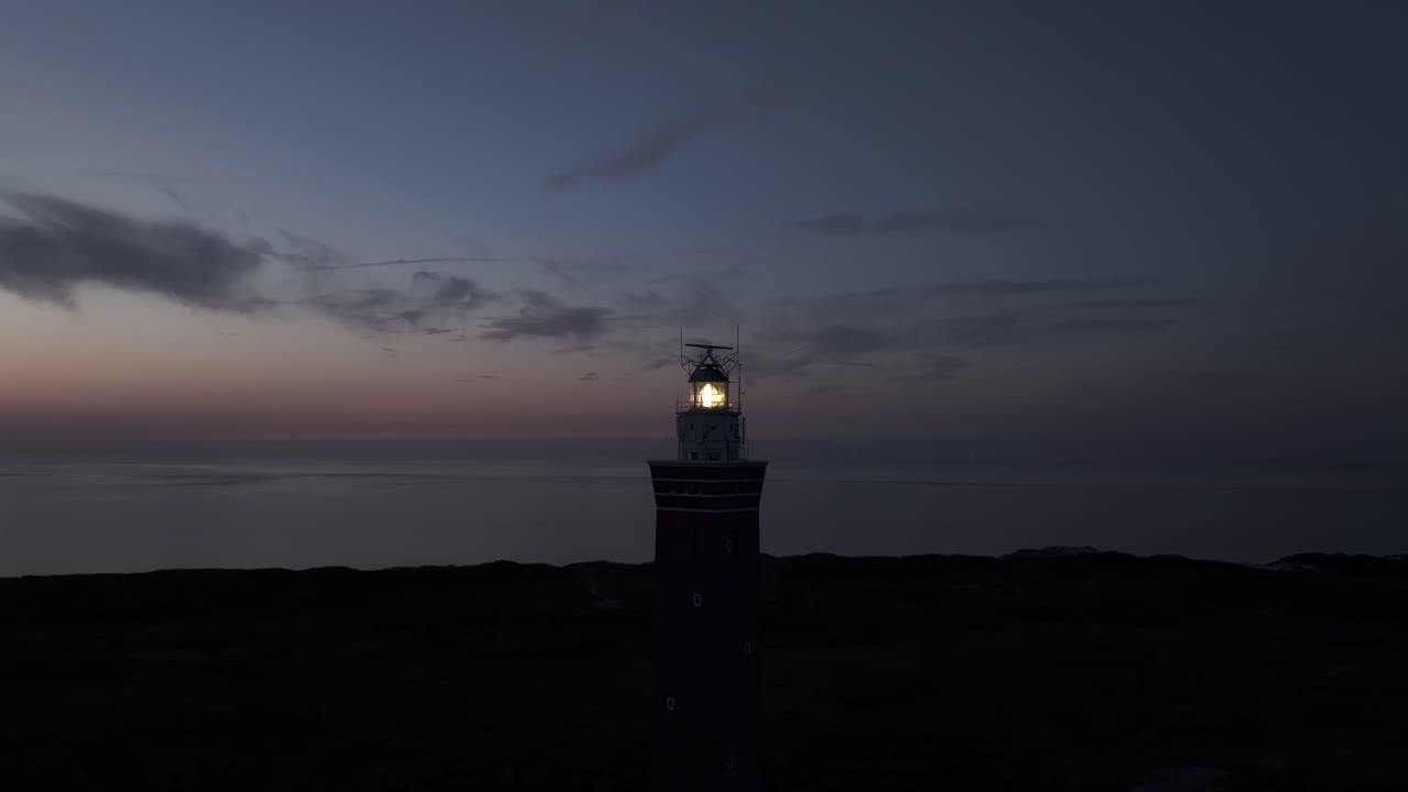 Vista aerea del faro di Westhoofd al tramonto con una calda luce dorata sulla spiaggia sabbiosa e le dune ondulate
