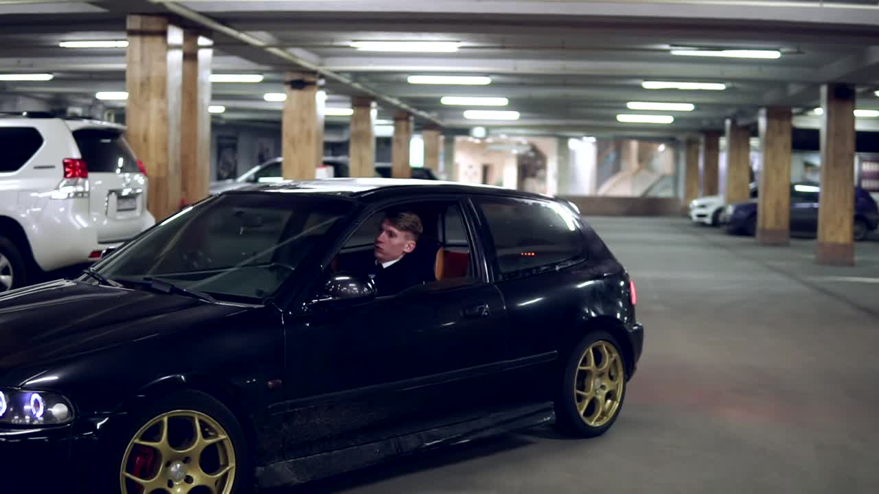 Businessman in a suit gets out of a black executive car in a garage parking lot, taks his black leather bag and goes away