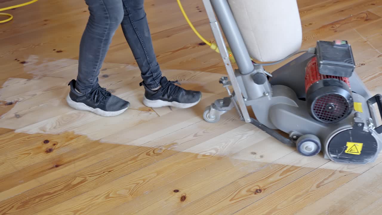 Worker operates floor sanding machine across hardwood flooring removing old finish