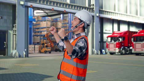 side view of asian male engineer with safety helmet screaming goal celebrating working , outside of logistics distributions warehouse