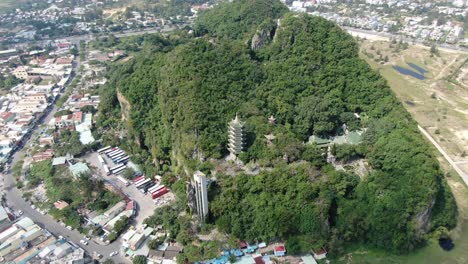 Drone-aerial-view-in-Vietnam-flying-over-Da-Nang-city-marble-mountains-full-of-trees-with-buddhist-temples-surrounded-by-flat-land-on-a-sunny-day