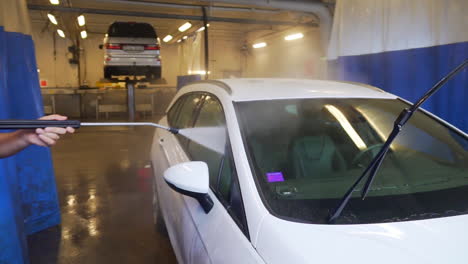 trabajador rociando agua y lavando las ventanas, de un automóvil todoterreno blanco, en un lavadero de automóviles, en suecia