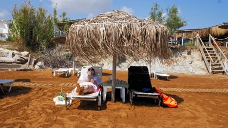 una turista relajada en una tumbona con dosel de juncos en la playa de megas lakkos, cefalonia, grecia - toma estática