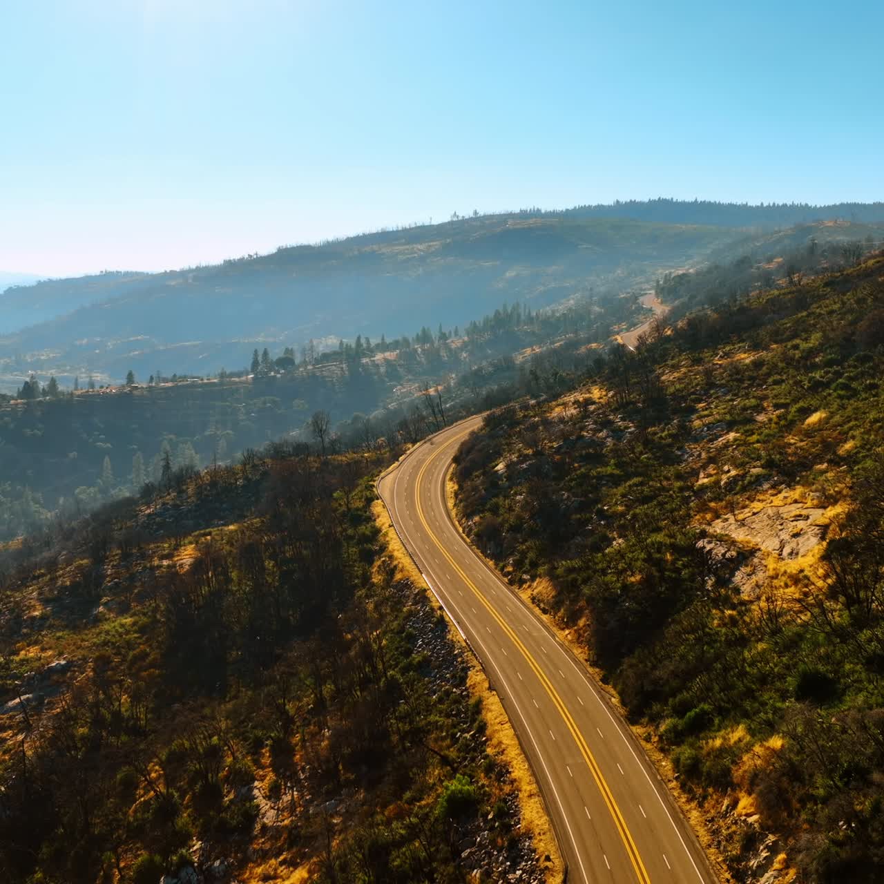 Flying above the sunlit highway in the mountains. Sunny day footage in Sierra National Forest, California, USA