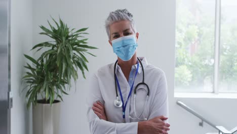 retrato de una mujer caucásica médica mayor con máscara de cara de pie con los brazos cruzados en el hospital
