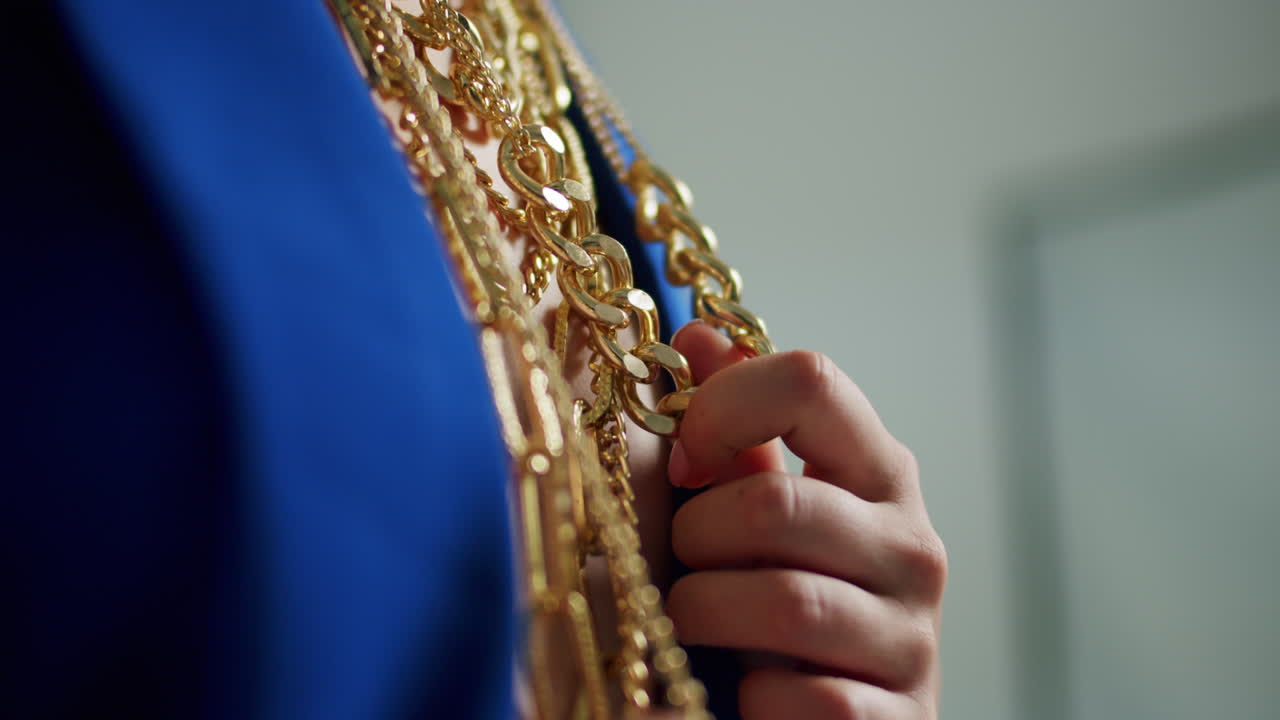 Donna con giacca blu che indossa e sistema diverse collane d'oro come simbolo di lusso e moda