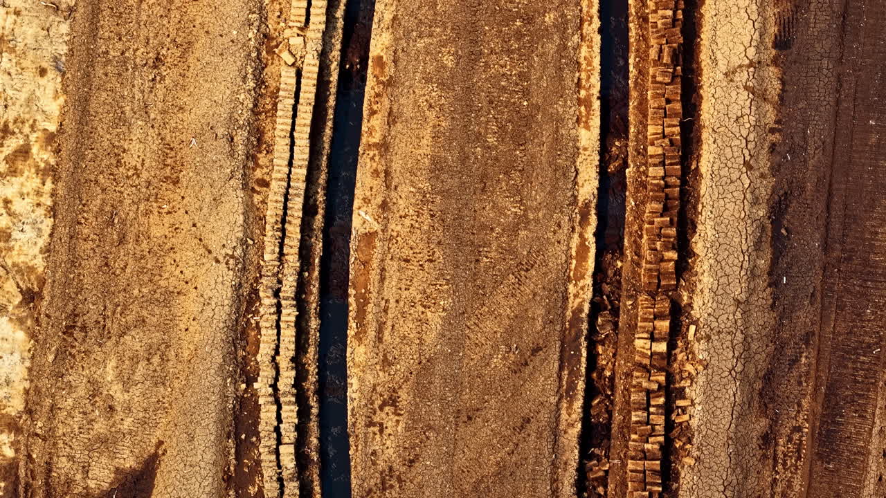 Stacks of harvested peat blocks dry in orderly rows across prepared field seen from above