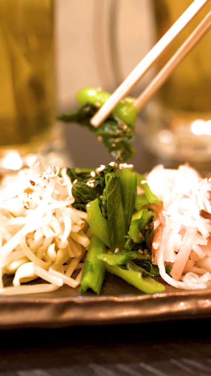 Primo piano di bacchette che raccolgono verdure condite da un piatto in un izakaya