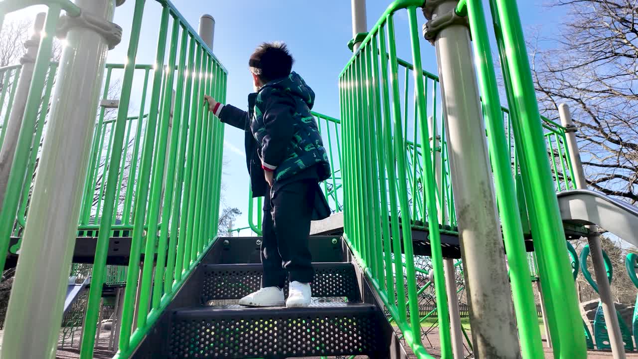 Barndomsudvikling og udendørs leg: Sydasiatisk dreng klatrer ned ad trapper på en legeplads i parken.