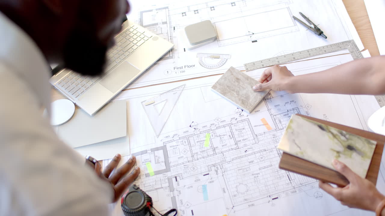 Reviewing architectural blueprints, diverse colleagues discussing design plans with laptop and mater