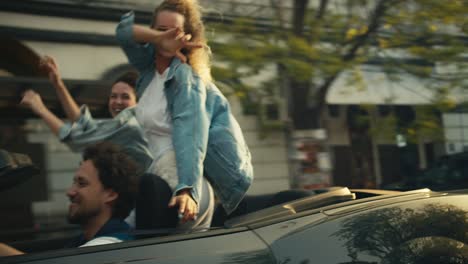 a blonde in sunglasses and a brunette are having fun while sitting in a gray convertible. happy car ride