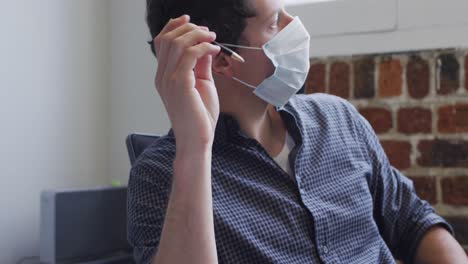 Man-wearing-face-mask-sitting-on-his-desk-at-office