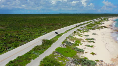 aerial of vehicle driving on empty island road with pristine white sand beaches on a sunny day