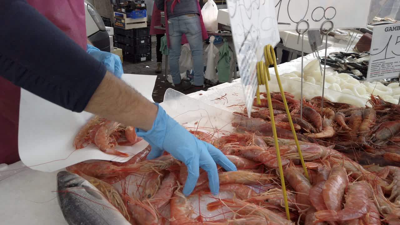 Un vendeur prend des crevettes rouges et les dépose sur une feuille de papier, vente de poisson au marché.
