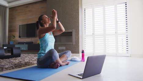 Mixed-race-woman-excercising-on-a-mat-with-laptop