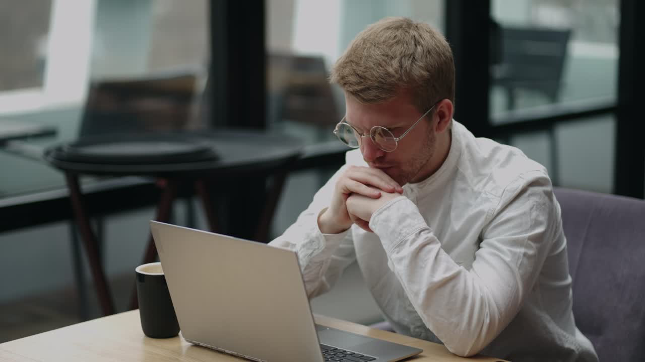 smart man with glasses is looking at display of laptop and thinking hard, concentrated office worker